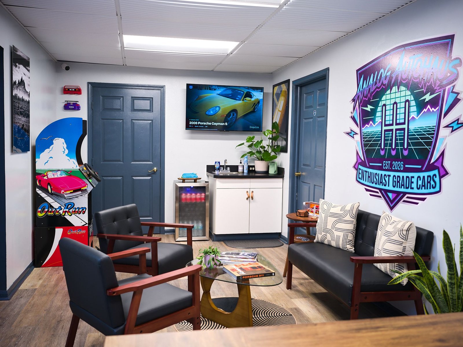 Analog Autohaus Office & Customer Lounge in Sarasota with Out Run arcade cabinet, drinks fridge, and Enthusiast Grade Cars logo wall